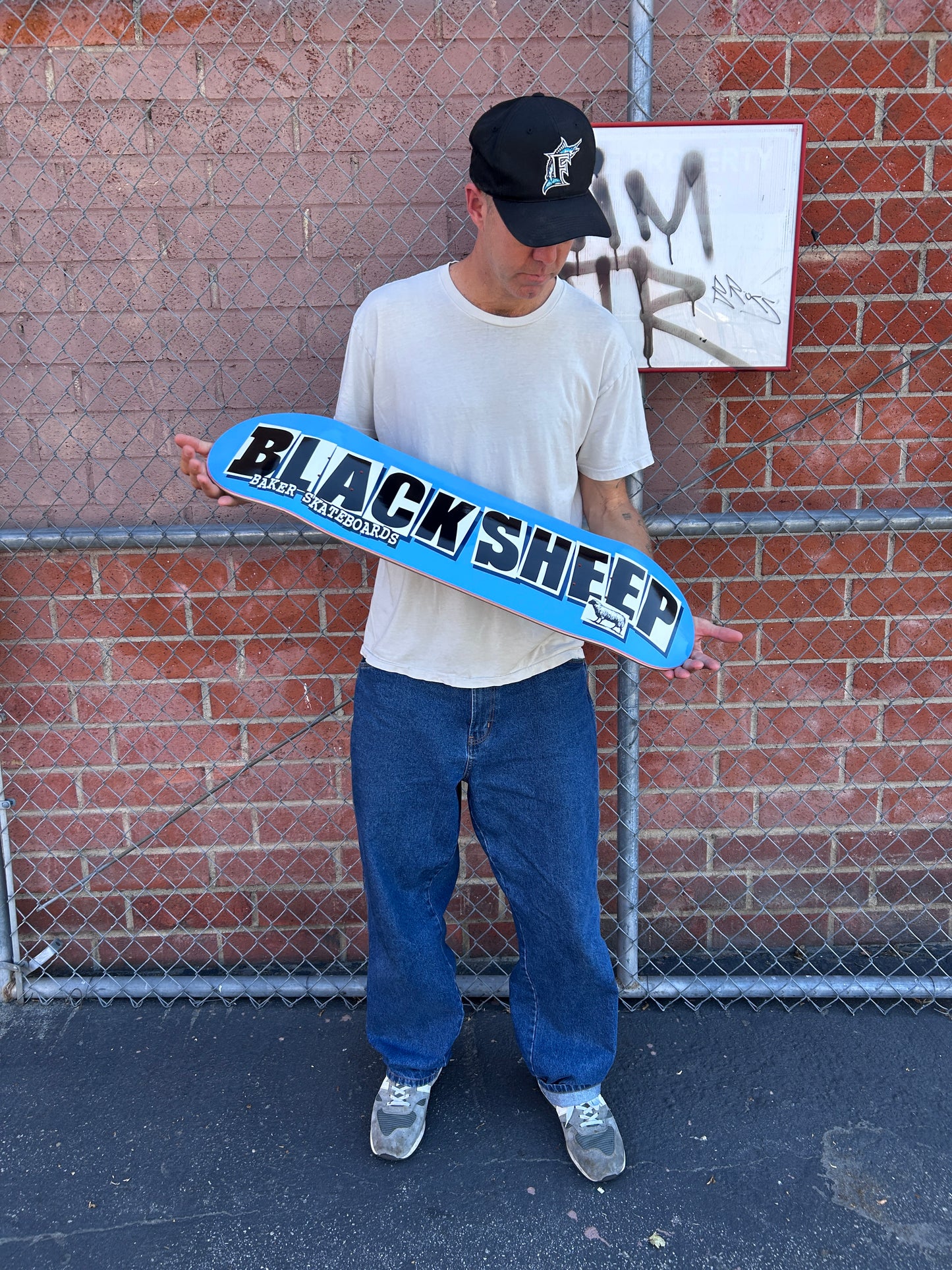 Person holding a blue skateboard with 'Black Sheep' branding on a brick pavement.