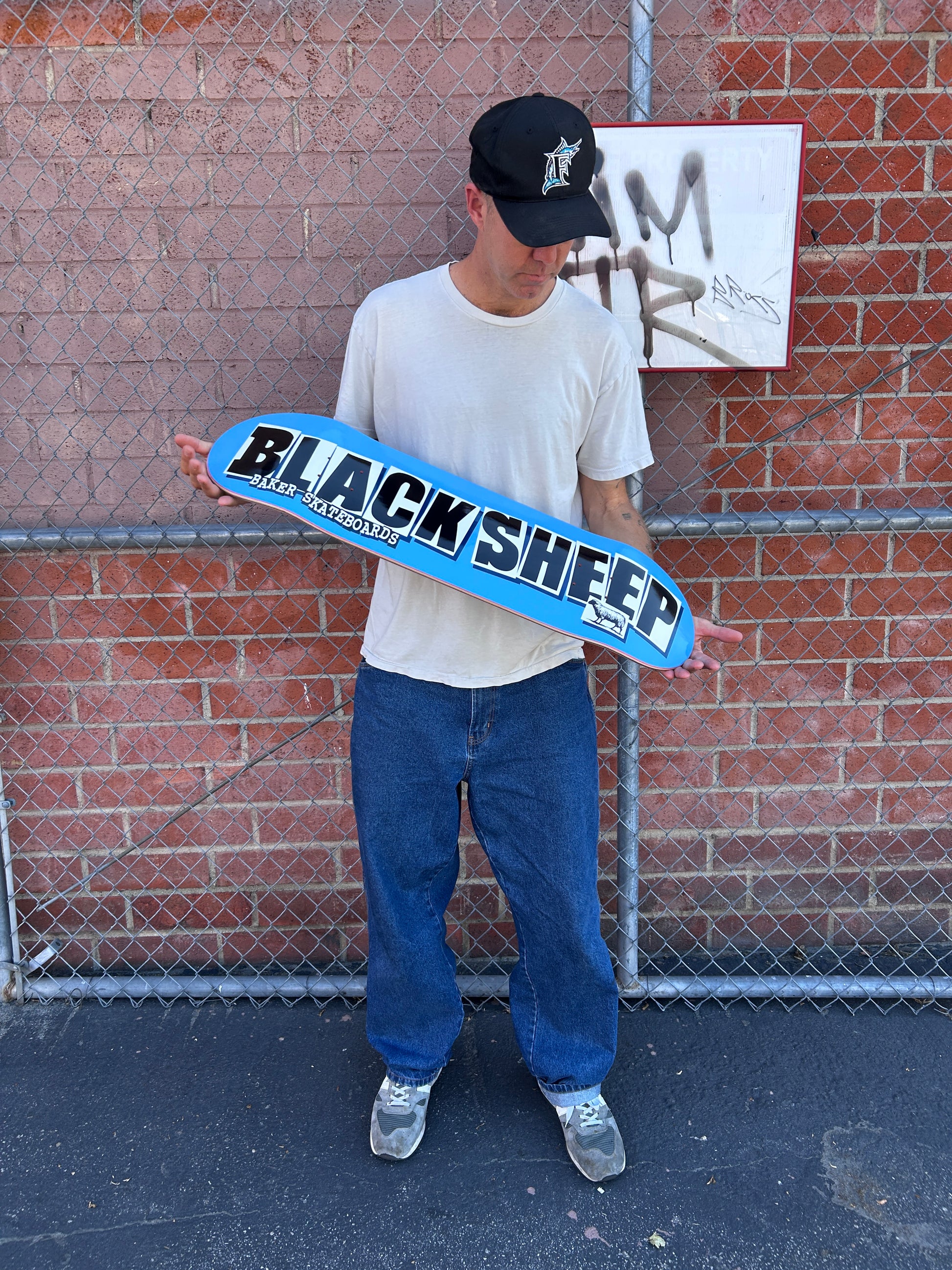 Person holding a blue skateboard with 'Black Sheep' branding on a brick pavement.