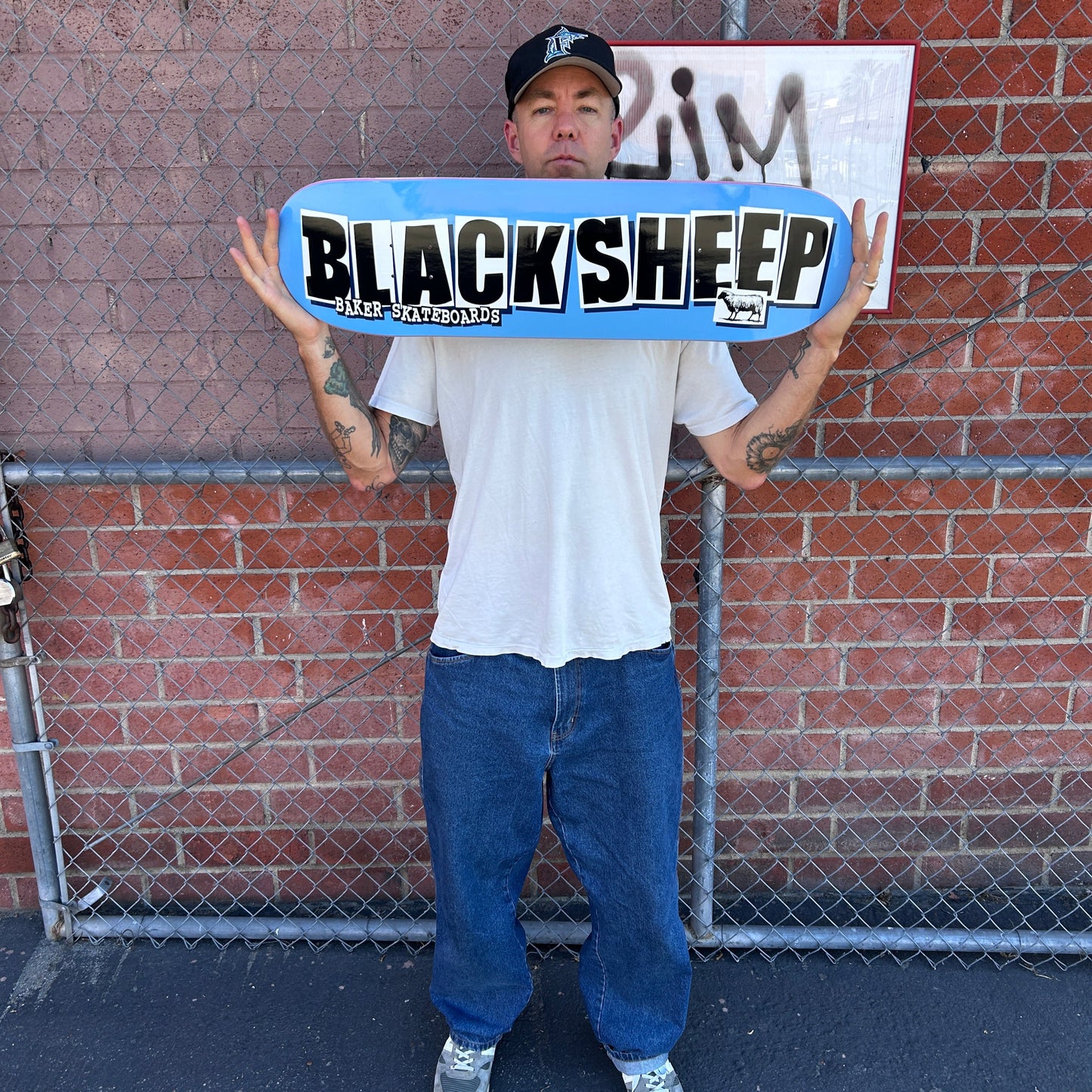 Person holding a skateboard with 'Black Sheep' branding on a brick pavement.